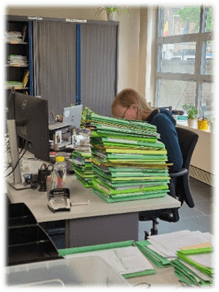 Medewerker overweldigd door stapels dossiers en administratie